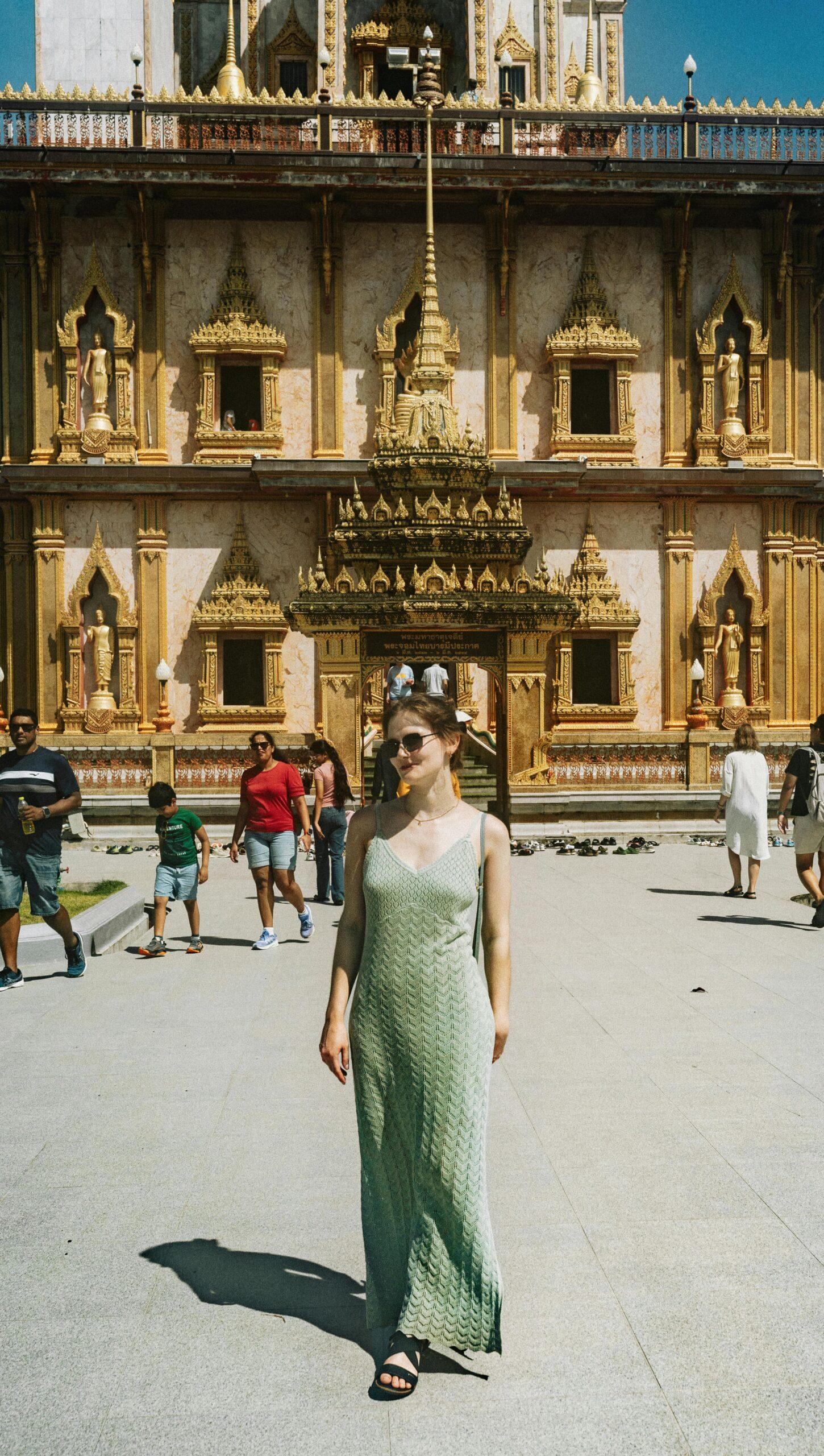 Woman in a green dress standing before Wat Chalong Temple in sunny Phuket.