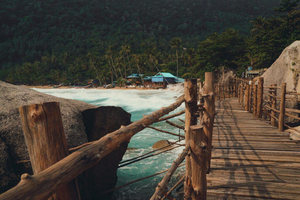 Rustic wooden pier with lush coconut trees and vibrant blue ocean waves on a tropical island beach.